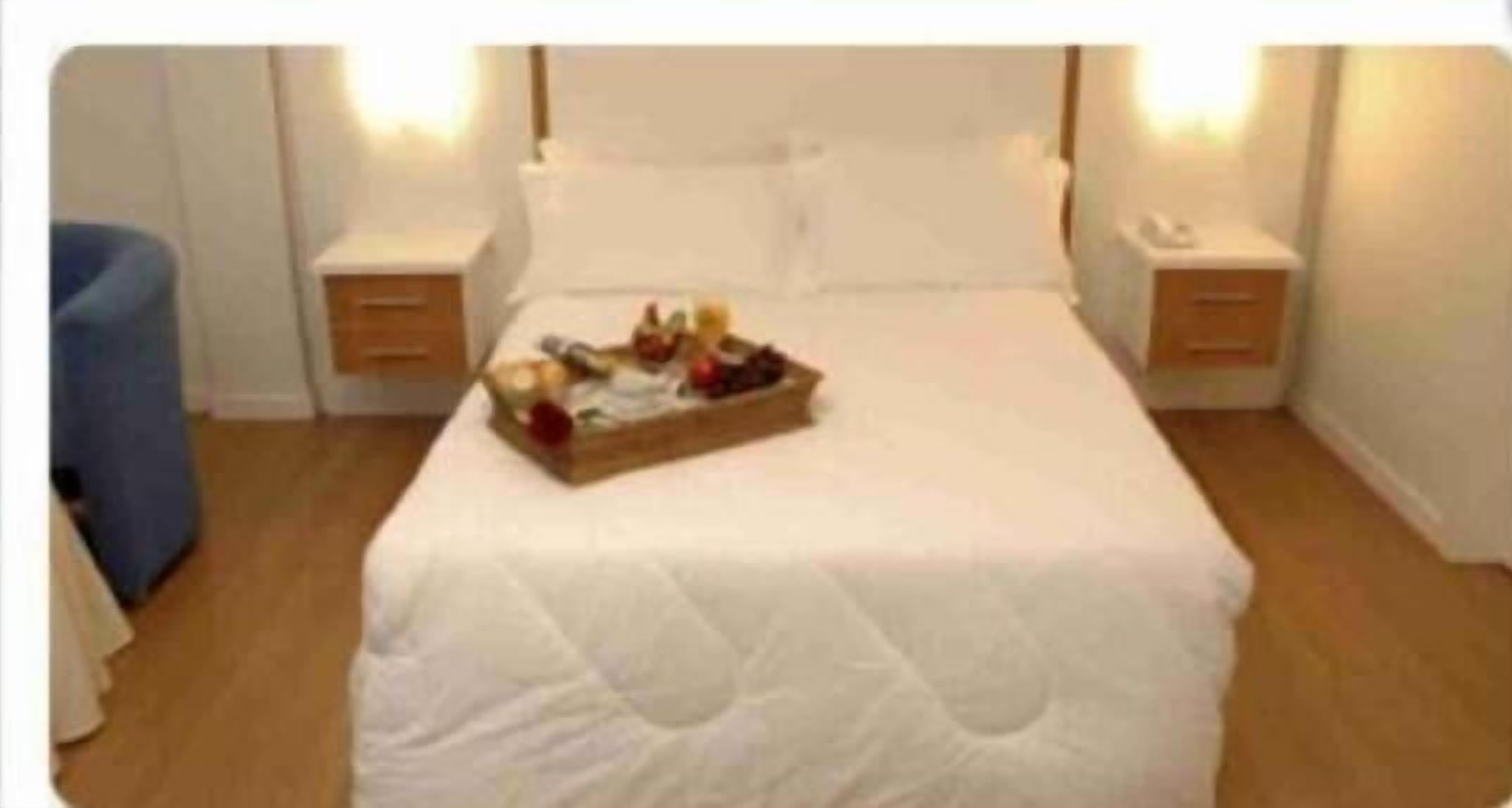 Una cama bien hecha con una bandeja de frutas y una botella de agua en el centro.