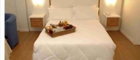 Una cama bien hecha con una bandeja de frutas y una botella de agua en el centro.