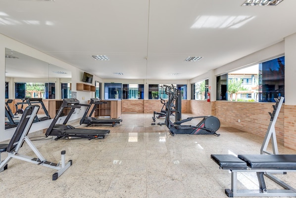 Ett gym med löpband, styrketräningsmaskiner och en vägg täckt med speglar.