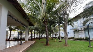 A hotel courtyard with palm trees, a paved walkway, and a building with a sign. - Diroma Lacqua V - Direto com o Grupo Diroma - Acesso ao Acqua Park com Café da Manhã (Caldas Novas)