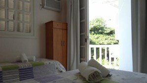 A bedroom with a bed, a wooden wardrobe, and a balcony with a view of greenery. - Pousada Belo Mar (Florianopolis)