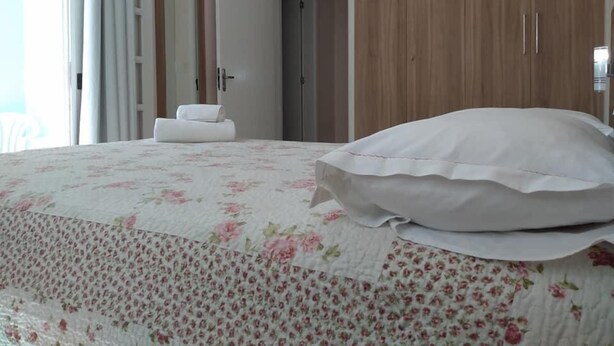 A bedroom with a bed, a wooden wardrobe, and a bathroom door. - Pousada Belo Mar (Florianopolis)