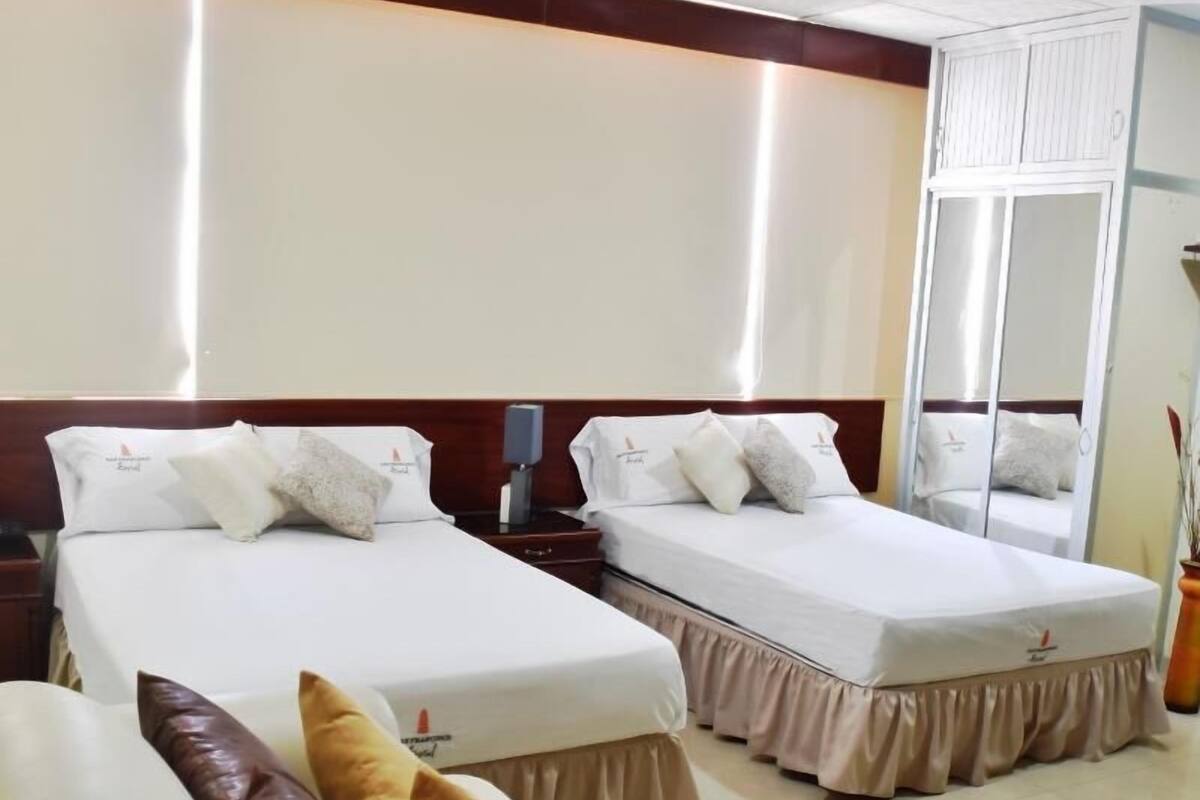 A hotel room with two beds, a nightstand, a mirror, and a potted plant.