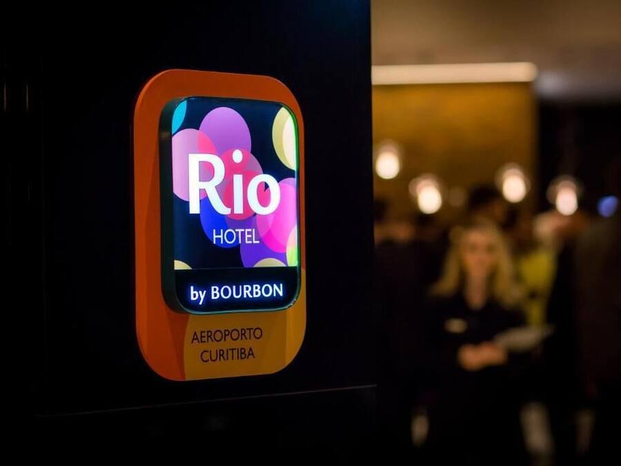 Placa do Hotel Rio by Bourbon, com um logotipo colorido e o nome 'AEROPORTO CURITIBA'.