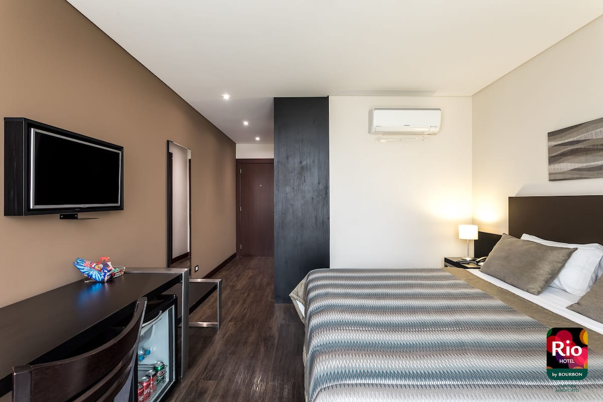 Une chambre d’hôtel équipée d’un lit, d’une table de chevet, d’une télévision et d’un mini-bar.