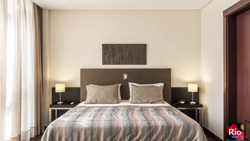 A hotel room with a large bed, two bedside tables with lamps, a headboard with a cityscape artwork, and a view of the city through the window.