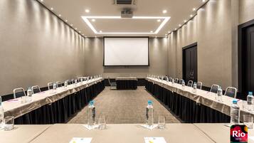 Un salón de conferencias con una larga mesa, sillas, botellas de agua y una pantalla de proyector.