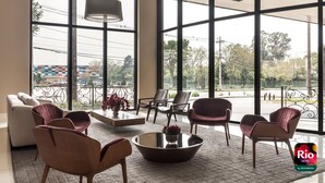 Une pièce spacieuse avec de grandes fenêtres, un canapé, des fauteuils, une table basse et une lampe.