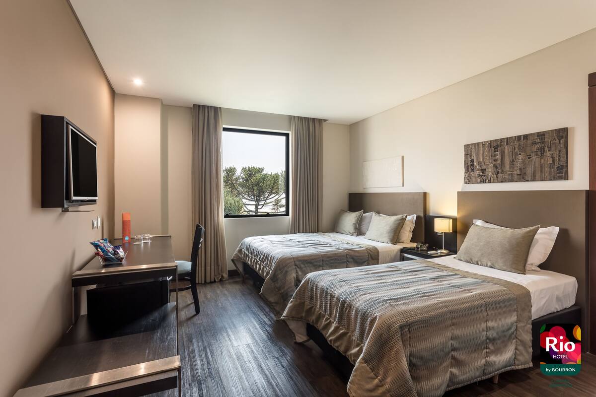 Une chambre d’hôtel avec deux lits, un bureau, une télévision et une fenêtre avec des rideaux.