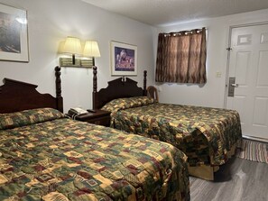 A hotel room with two beds, a nightstand, a lamp, a framed picture, and a door. - Mustang Motel Gillette I-90 (Gillette)