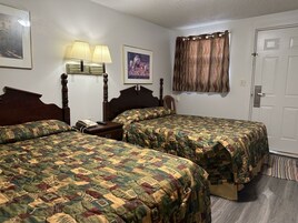 A hotel room with two beds, a nightstand, a lamp, a framed picture, and a door.