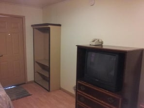 A room with a wooden wardrobe, a television on a wooden stand, and a door. - Mustang Motel (Gillette)