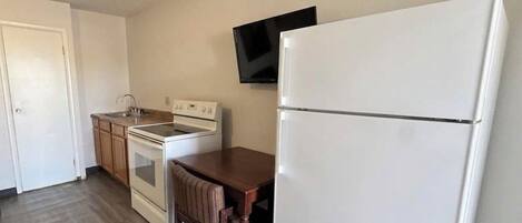 Una cocina con un refrigerador blanco, una estufa, un lavamanos y un televisor montado en la pared.