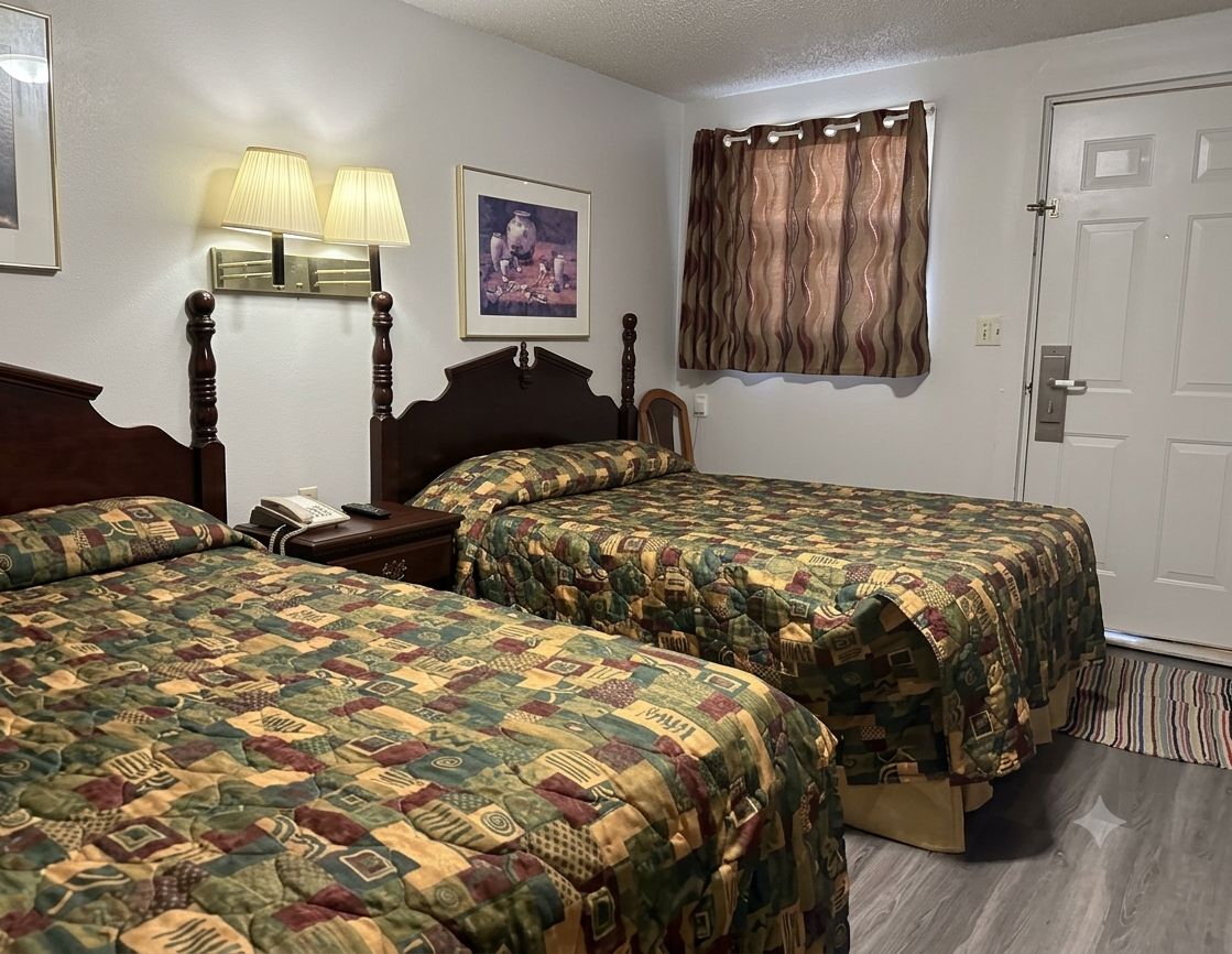 A hotel room with two beds, a nightstand, a telephone, a lamp, a picture on the wall, a window with curtains, and a door.