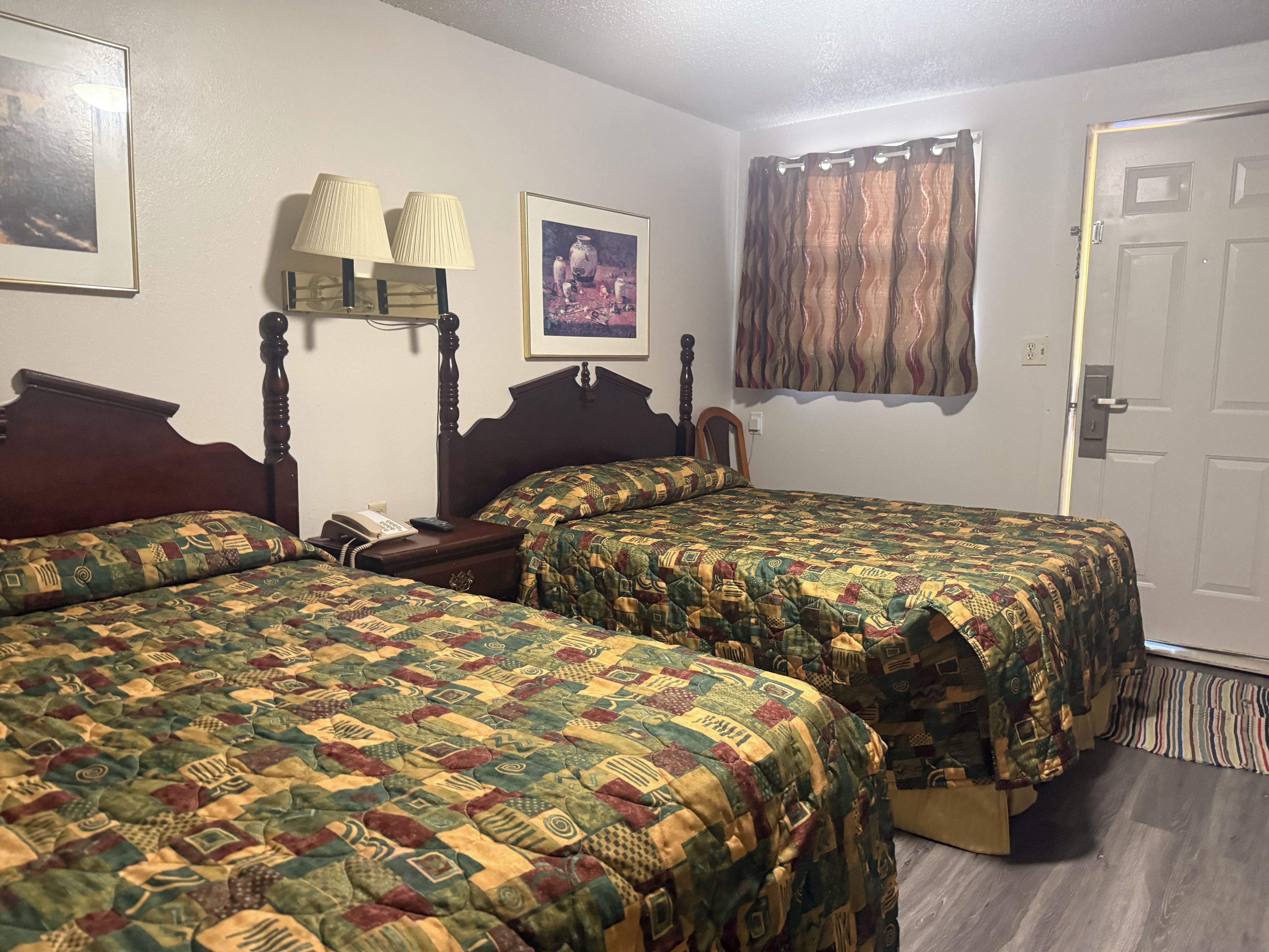 A hotel room with two beds, a bedside table with a lamp, a telephone, and a framed picture on the wall.