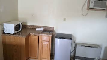 A compact kitchen with a microwave, refrigerator, and air conditioning unit.