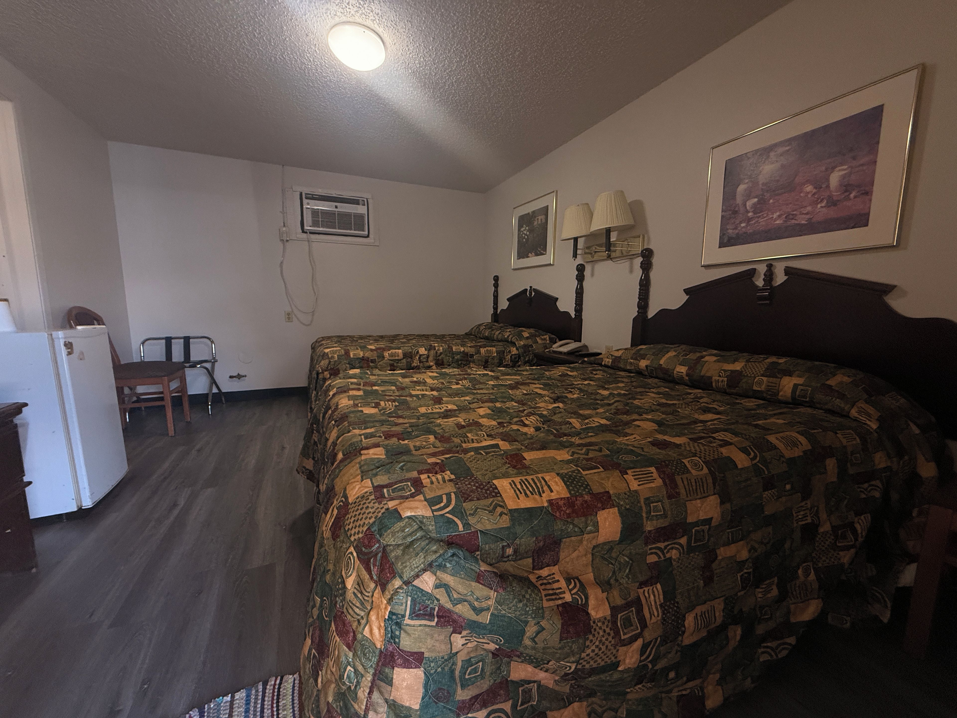 Een slaapkamer met een groot bed, een bureau, een stoel, een koelkast en een schilderij aan de muur.