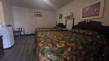 Een slaapkamer met een groot bed, een bureau, een stoel, een koelkast en een schilderij aan de muur.