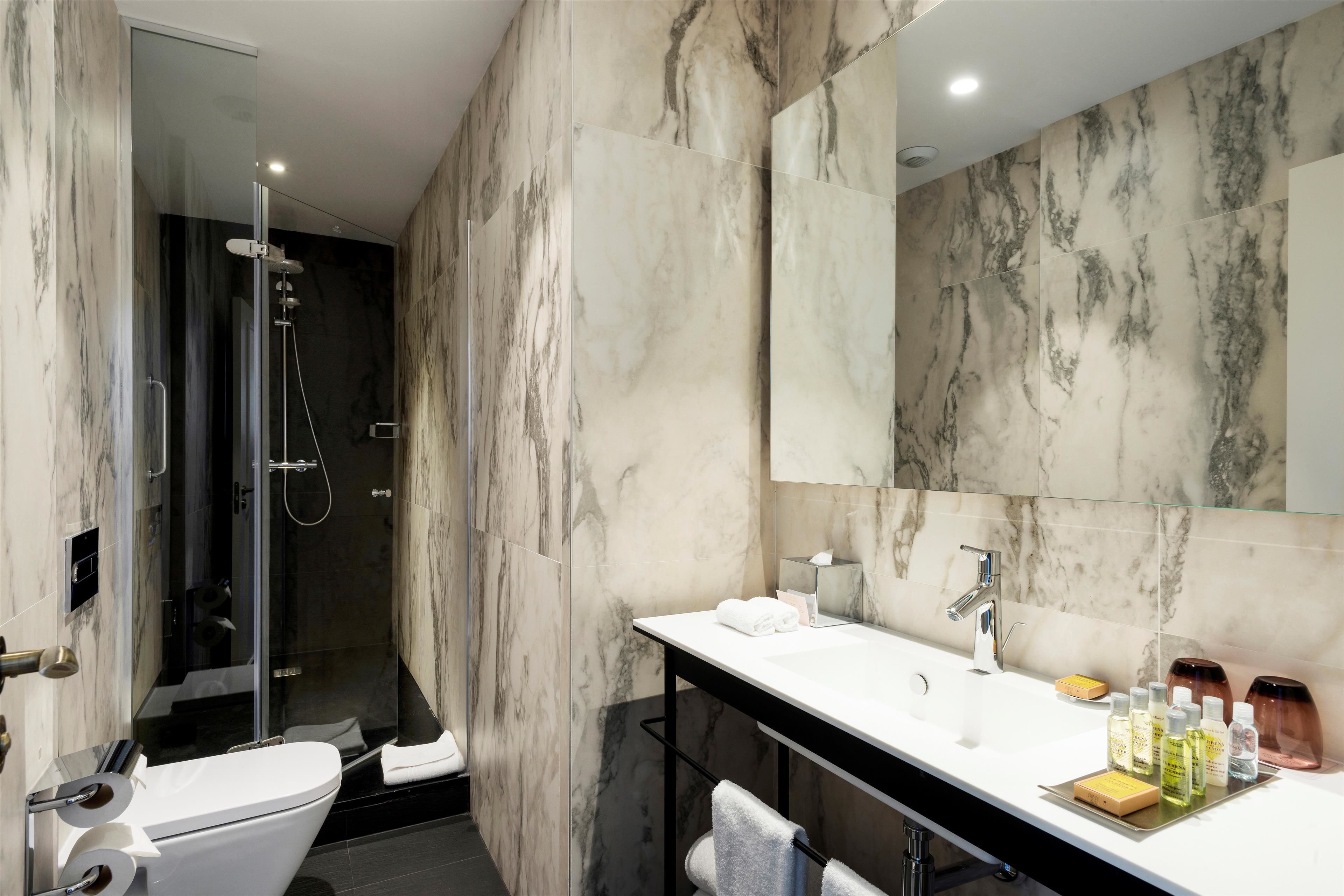 A modern bathroom with a glass-enclosed shower, a white sink with a marble countertop, and a large mirror.