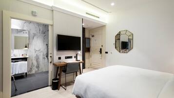 A modern hotel room with a large bed, a desk with a chair, a television, and a bathroom with a marble wall and a sink.