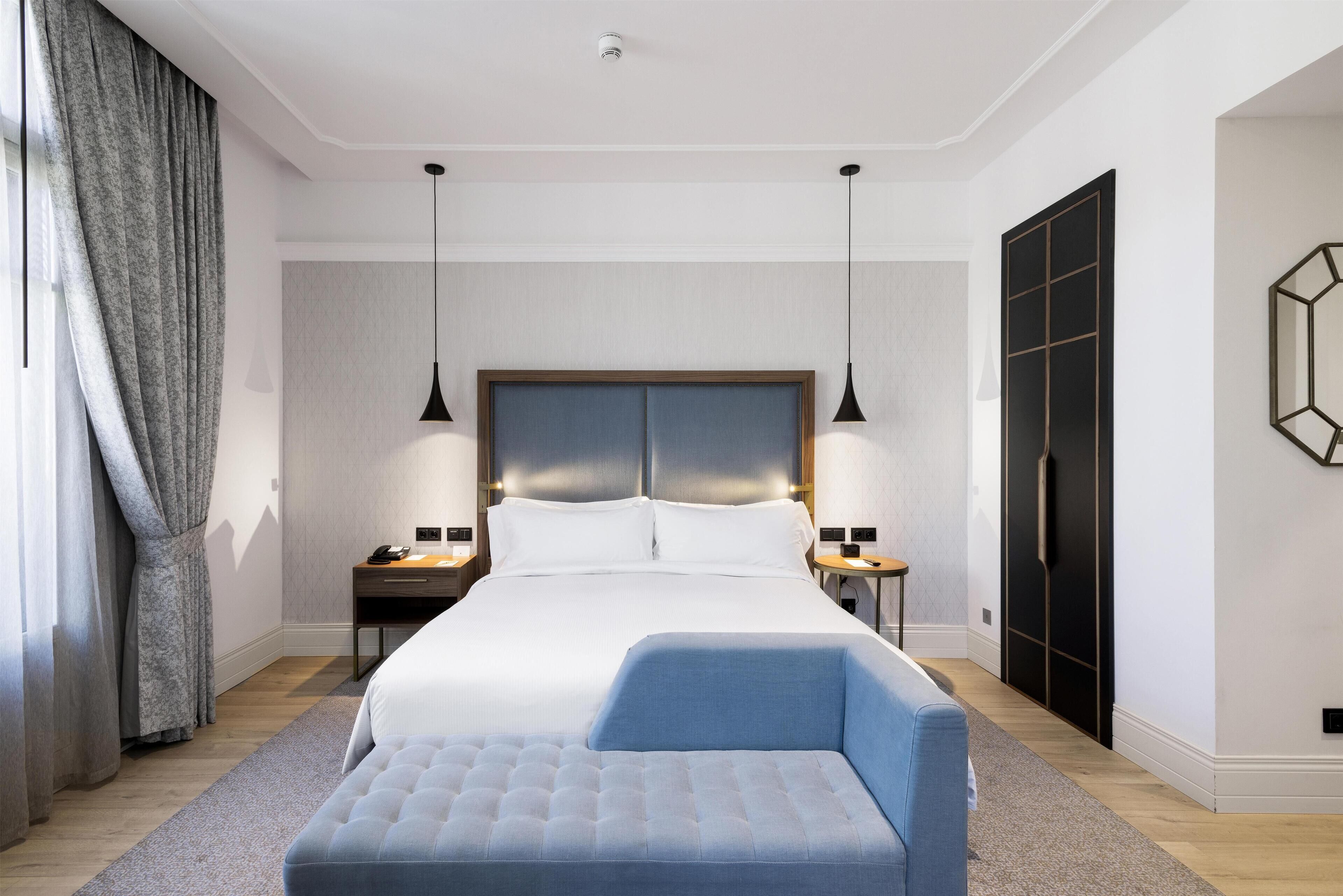 Una habitació d'hotel moderna amb un llit gran, taules de nit, un escriptori i un armari.