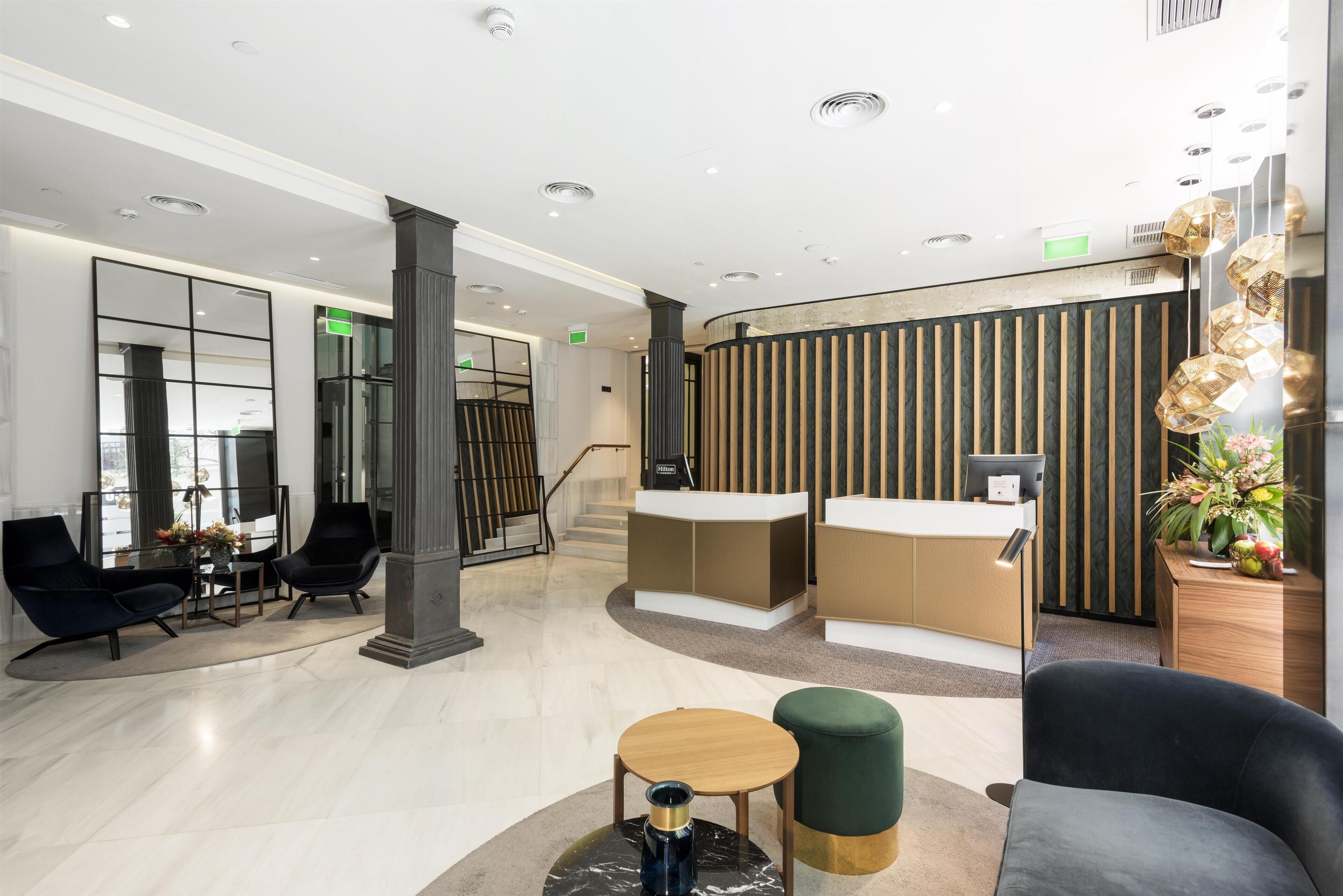 A modern lobby with a reception desk, seating area, and a staircase.