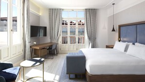 A modern hotel room with a large bed, a desk, a TV, and a view of a balcony. - DoubleTree by Hilton Madrid-Prado (Madrid)