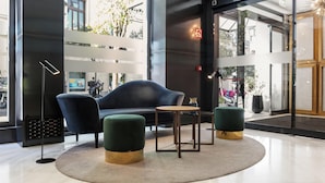 A modern lobby with a black leather sofa, a round wooden table, and two green ottomans. - DoubleTree by Hilton Madrid-Prado (Madrid)
