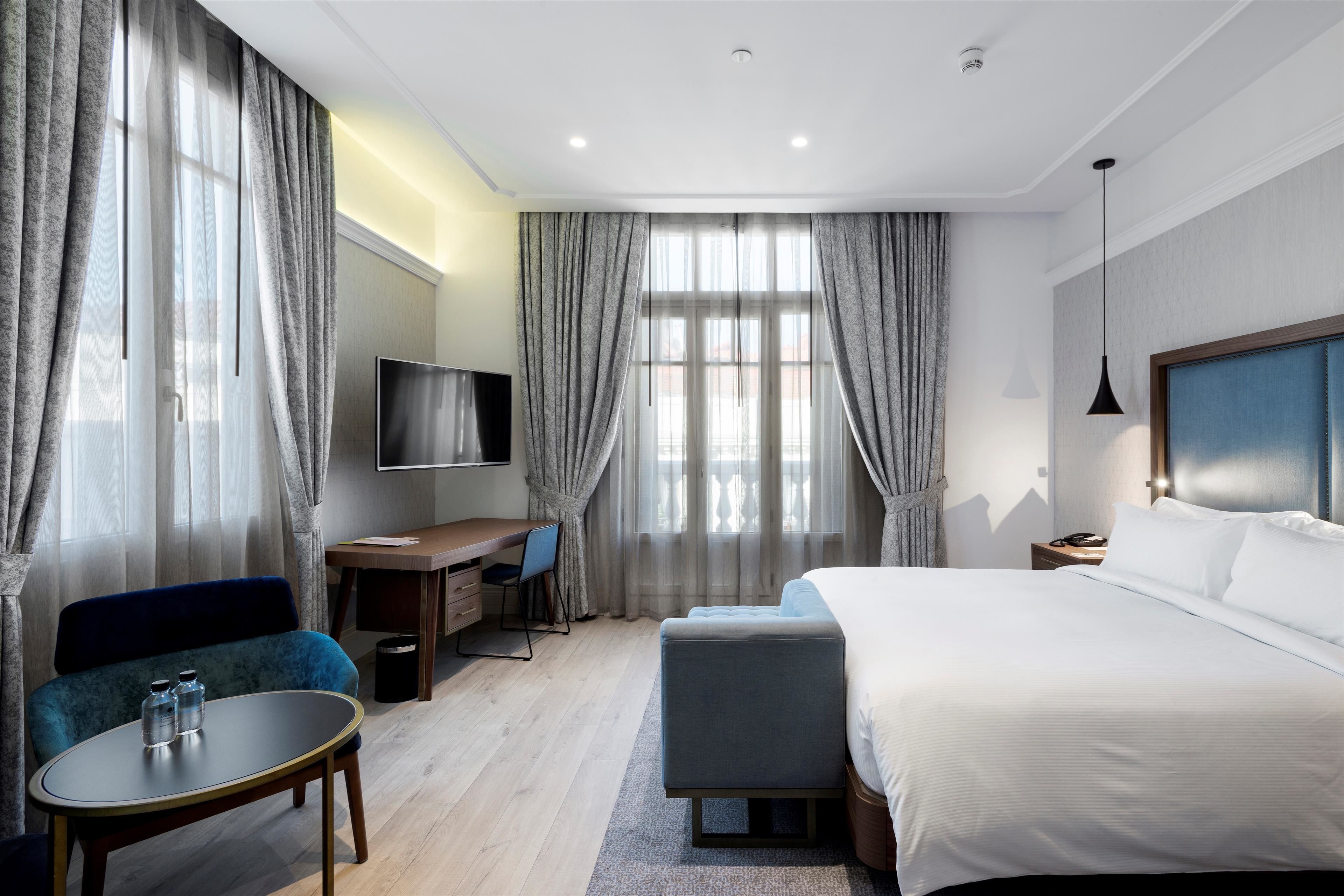 Ein modernes Hotelzimmer mit einem großen Bett, einem Schreibtisch mit Stuhl, einem Fernseher und einem Sofa.