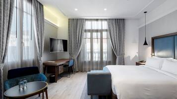 Ein modernes Hotelzimmer mit einem großen Bett, einem Schreibtisch mit Stuhl, einem Fernseher und einem Sofa.