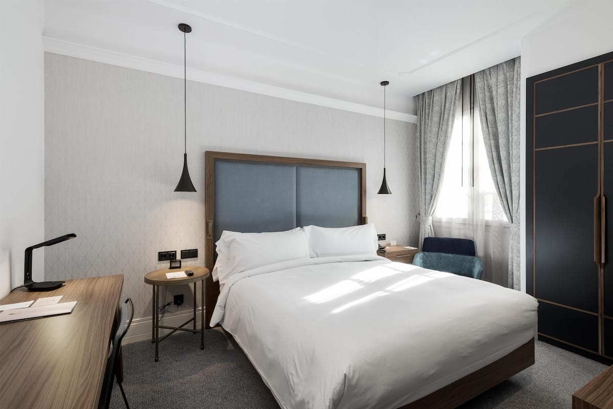 A hotel room with a large bed, bedside tables, a desk, and a wardrobe.