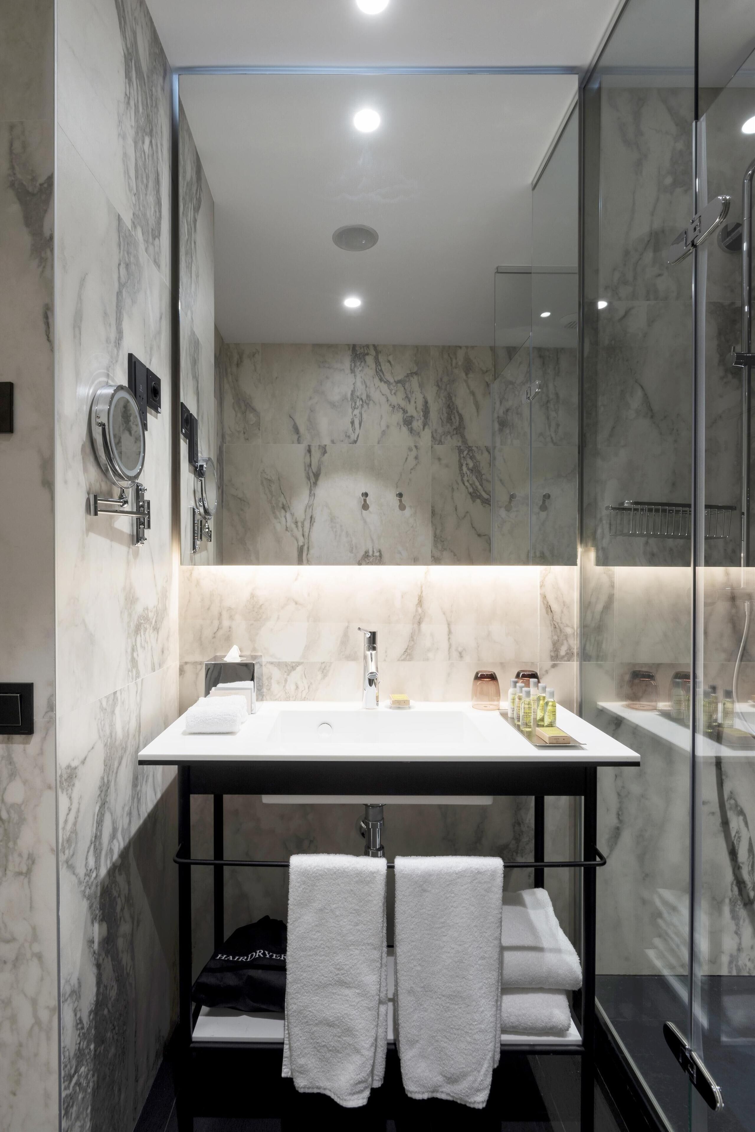A modern bathroom with a marble backsplash, a glass shower enclosure, and a vanity with a mirror and towel rack.