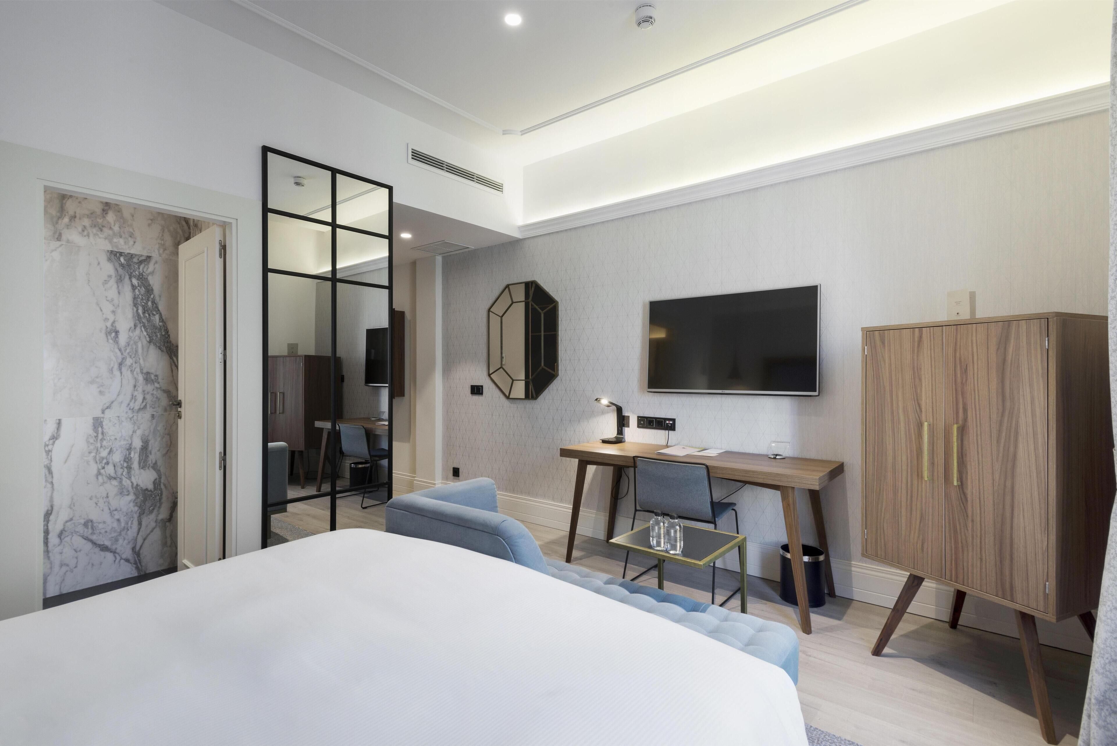 Quarto de hotel moderno com uma cama grande, uma escrivaninha, uma cadeira, uma televisão e um guarda-roupa.