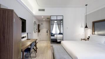 Una habitación de hotel moderna con un escritorio de madera, una cama grande, un televisor y vistas a través de un ventanal.