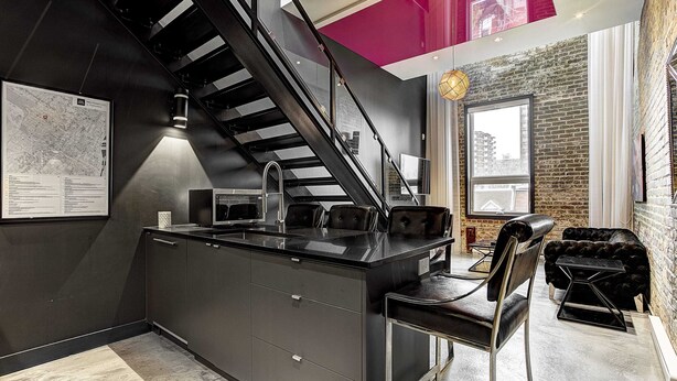 A modern kitchen with a central island, a black staircase, and a dining area with a black leather sofa. - Hotel Milton-Parc (Montreal)