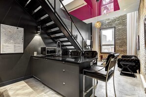 Una cocina moderna con una isla central, una escalera negra y un comedor con un sofá de cuero negro.