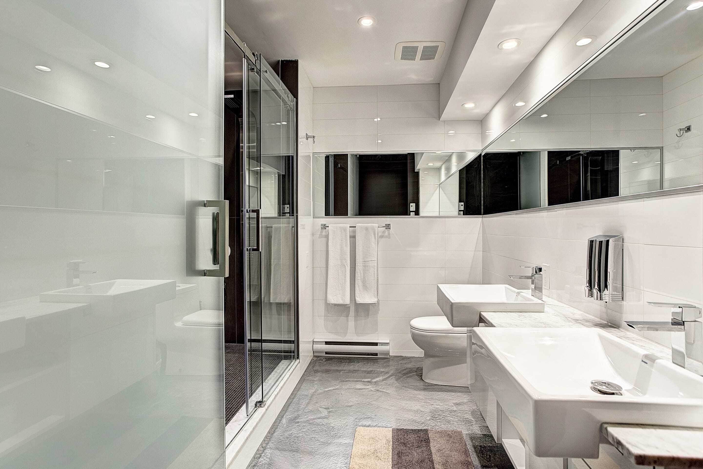 A modern bathroom with a glass shower enclosure, a toilet, and a vanity with a mirror.