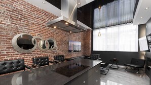 A modern kitchen with a brick wall, a central island with a stovetop, black leather seating, and a large window with sheer curtains. - Hotel Milton-Parc (Montreal)