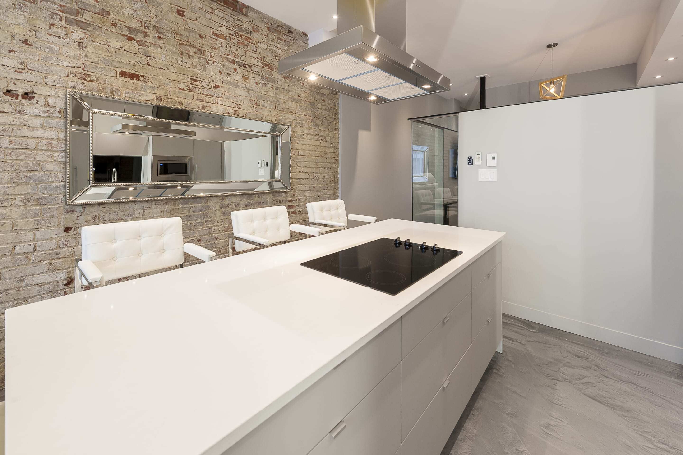 A modern kitchen with a large island, white cabinetry, and a brick accent wall.