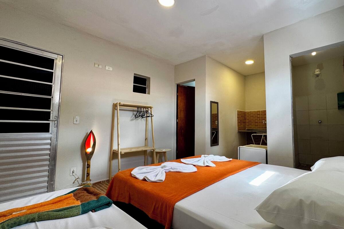 Ein Hotelzimmer mit zwei Betten, einem Wäscheständer aus Holz, einem Spiegel und einem kleinen Badezimmer, das durch eine geöffnete Tür sichtbar ist.