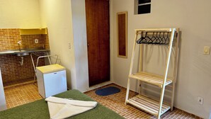 A compact bathroom with a sink, a small refrigerator, a wooden door, a drying rack, and a blue mat on the floor. - Pousada Maresia Centro (Ipojuca)