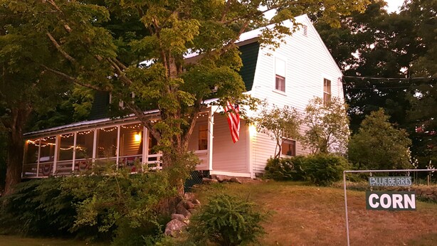 A white house with a porch, surrounded by trees and a sign indicating 'Blueberries' and 'Corn'. - The Farmstand Bed & Breakfast (Chocorua)