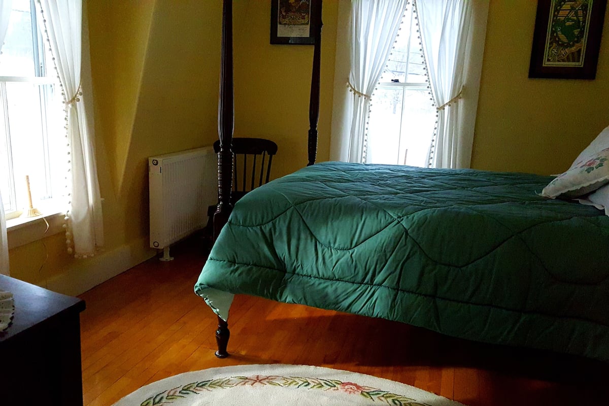 Une chambre à coucher avec un lit, un radiateur, une chaise et une table recouverte d’une nappe en dentelle.