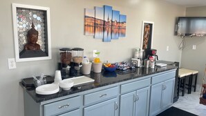 A modern kitchen with a marble countertop, a built-in sink, and light blue cabinets. There are two coffee makers, a fruit bowl, and a decorative Buddha statue. - Viking Motel (Lindsborg)