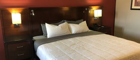 Quarto de hotel com uma cama grande, duas mesas de cabeceira e uma luminária fixada na parede.