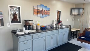 A modern kitchen with a marble countertop, a built-in sink, and a coffee station. There are cabinets with silver handles, a trash can, and a blue sofa in the living area. - Viking Motel (Lindsborg)