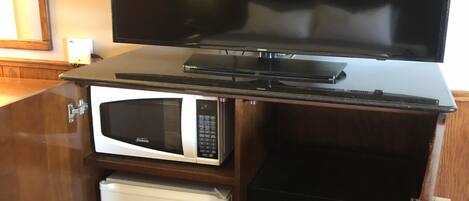A kitchen area with a microwave, a toaster, and a flat-screen TV on a wooden cabinet.