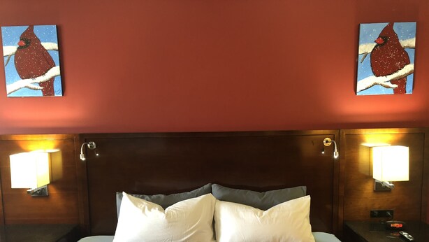 A hotel room with a large bed, two wall-mounted lamps, and two paintings of birds on the walls. - Viking Motel (Lindsborg)