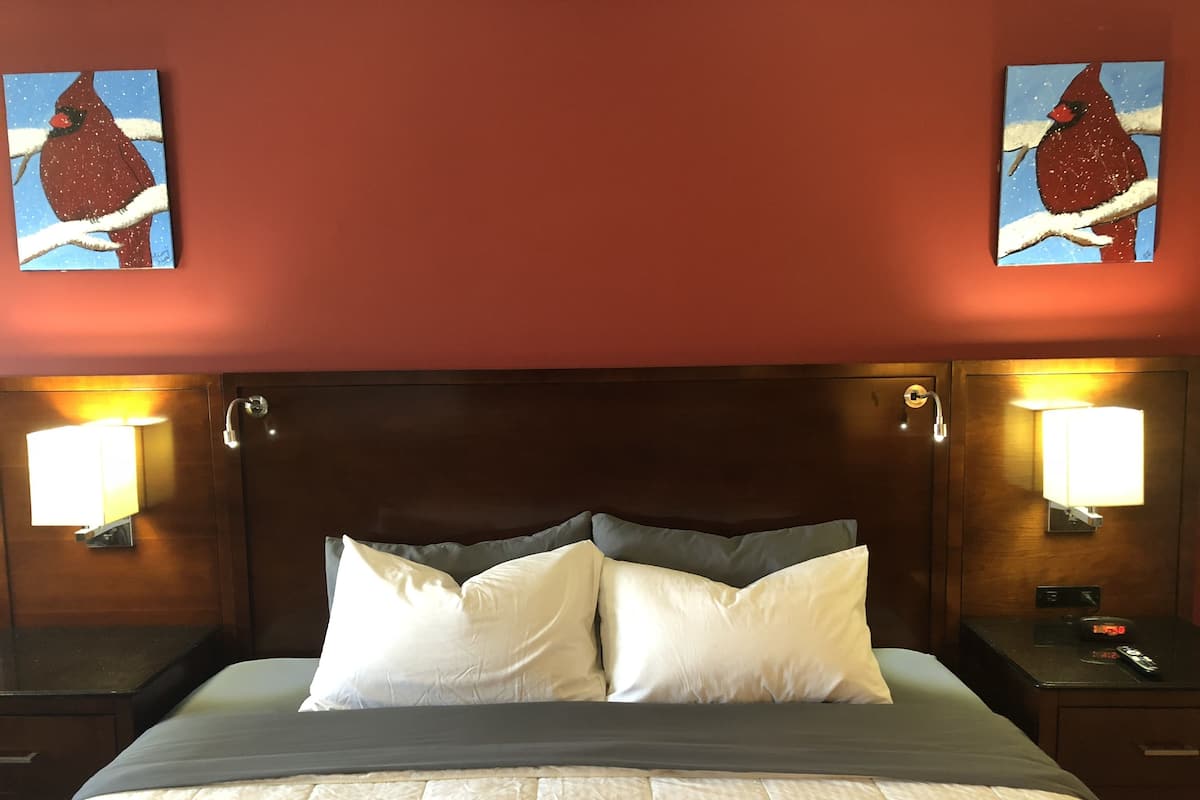 A hotel room with a large bed, two wall-mounted lamps, and two paintings of birds on the walls.