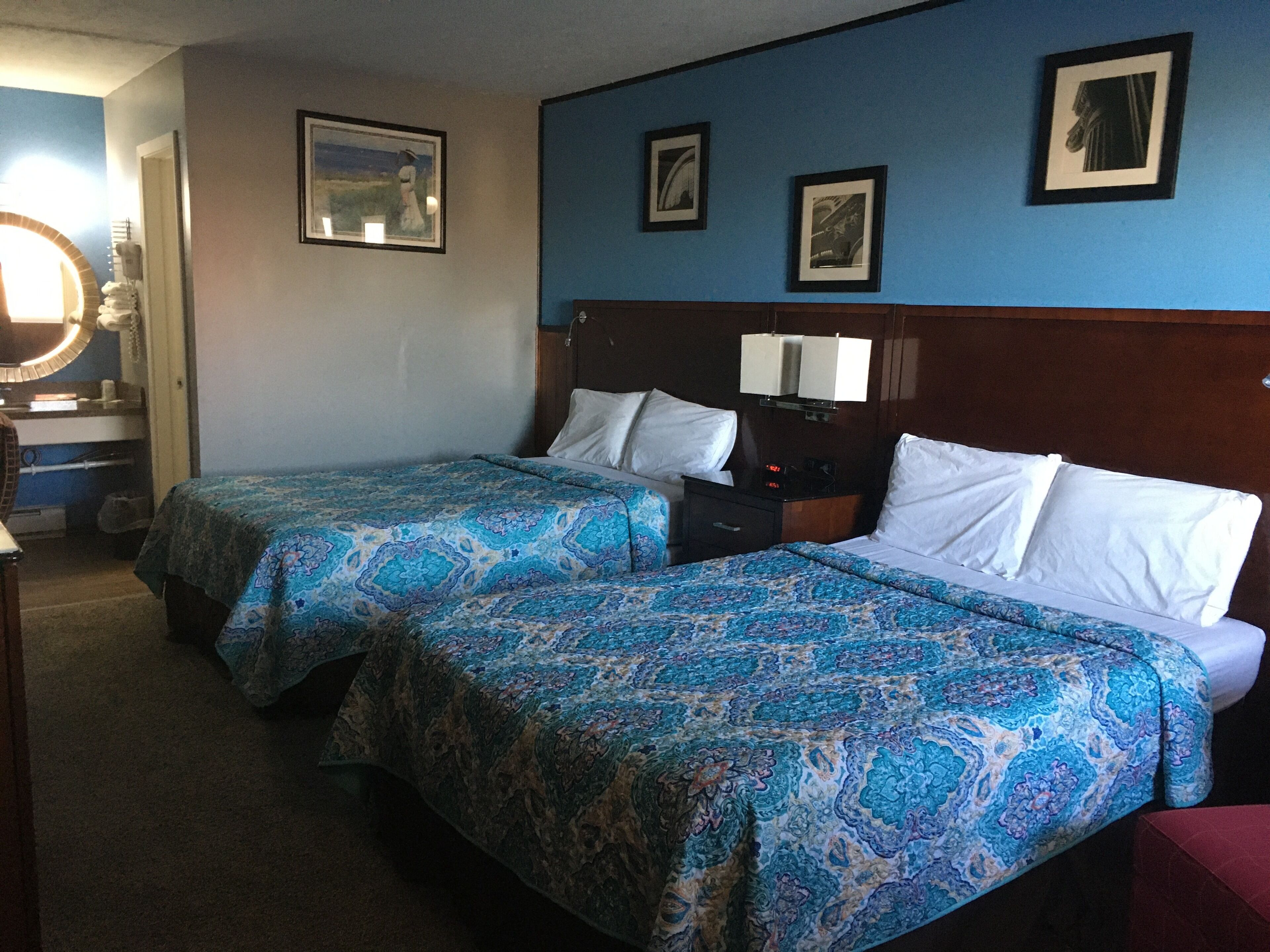 A hotel room with two beds, a nightstand, a mirror, and framed pictures on the wall.